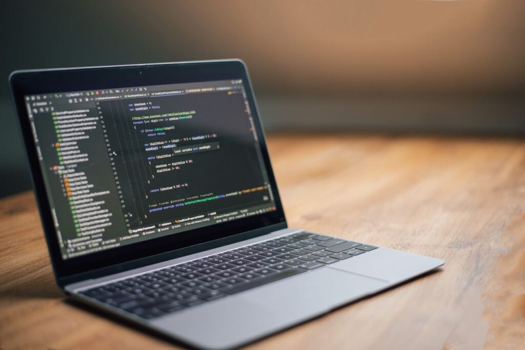 Laptop displaying software code on a wooden table, ideal for tech and programming themes.
